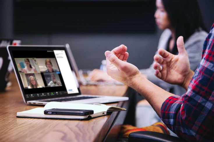 A person participating in a video conference on a laptop during a business meeting, with notebook and smartphone on the table, symbolizing remote team collaboration.